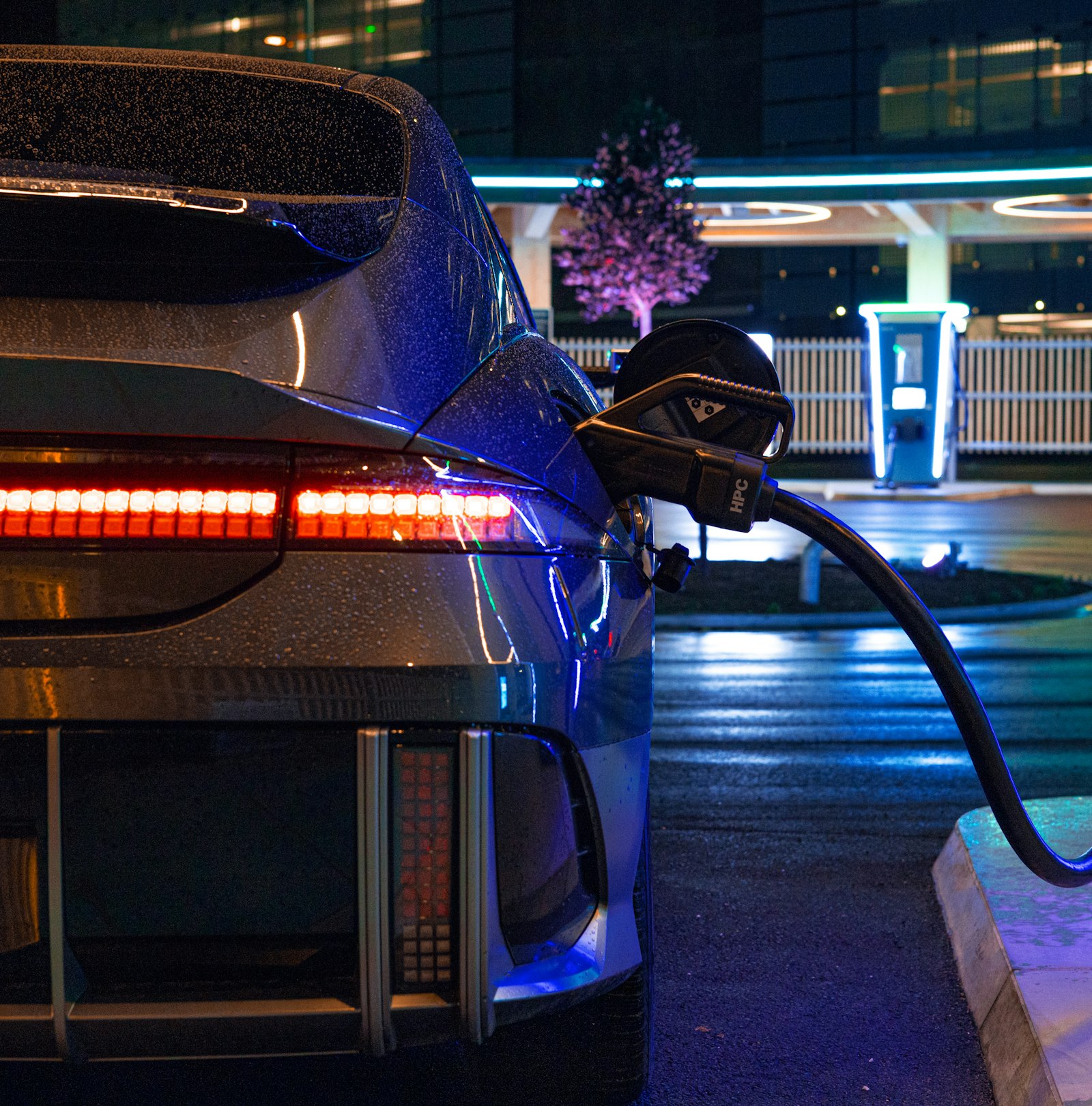 Gece aydınlık bir şarj istasyonunda şarj olan beyaz elektrikli Hyundai IONIQ 6